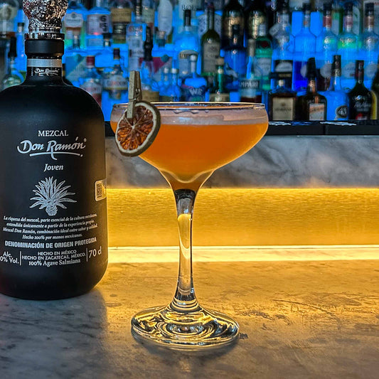 Naked & Famous cocktail in een gekoeld coupeglas, met rokerige mezcal, Aperol, gele Chartreuse en een schijfje limoen als garnish.