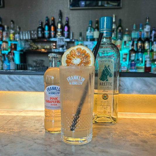 Cocktail recept: Paloma. Een frisse mix van tequila, limoen en grapefruit soda, geserveerd met ijs en een schijfje grapefruit.