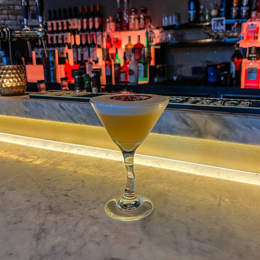 Pornstar Martini cocktail met vanille vodka, passievrucht en schuimlaag, geserveerd in een martiniglas met halve passievrucht als garnering. Cocktail Hotspots Recept