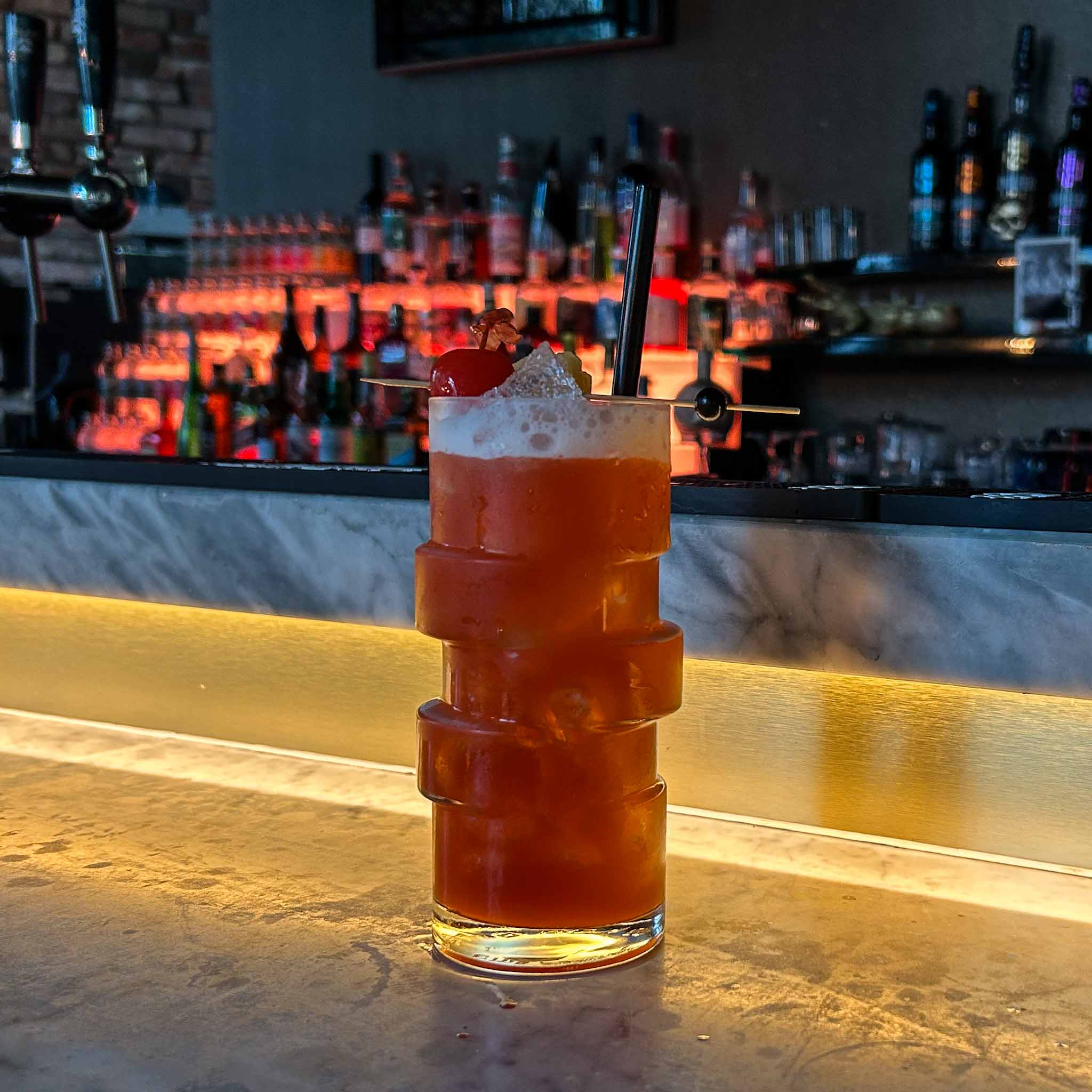 Singapore Sling cocktail met gin, kersenlikeur en ananas, geserveerd met ijs en garnering van ananas en kers.