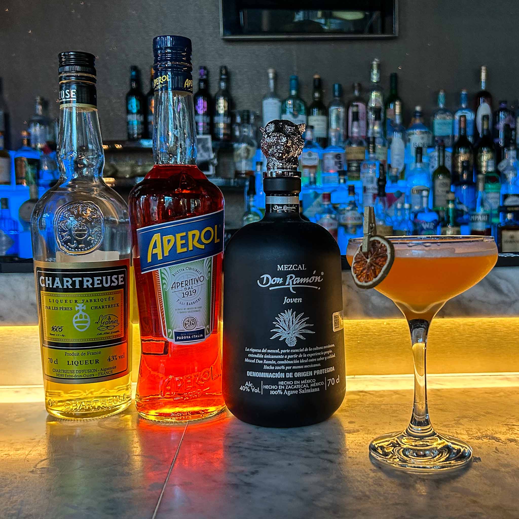 Naked & Famous cocktail in een gekoeld coupeglas, met rokerige mezcal, Aperol, gele Chartreuse en een schijfje limoen als garnish.